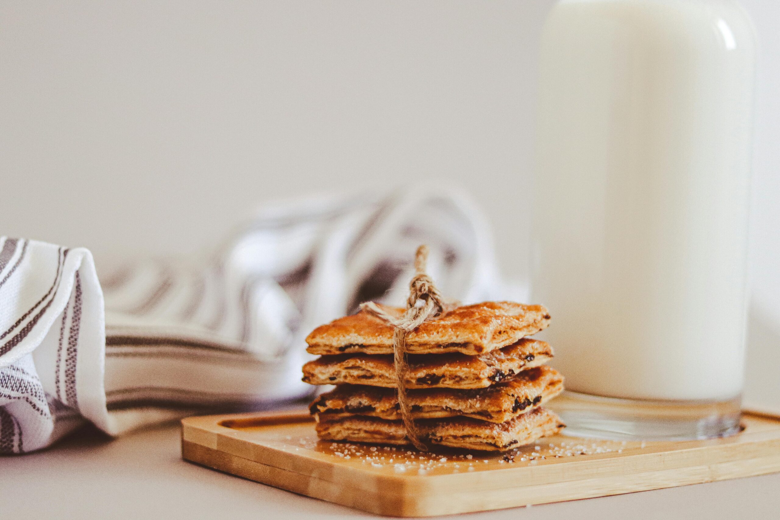 Stack of homemade cookies with a glass of milk on a wooden tray, creating a cozy, inviting atmosphere.