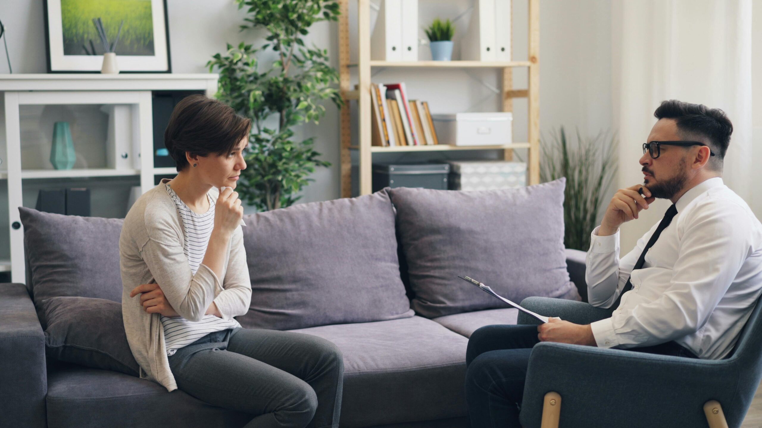 A therapist and client engage in a thoughtful session on a comfortable couch, fostering healing.