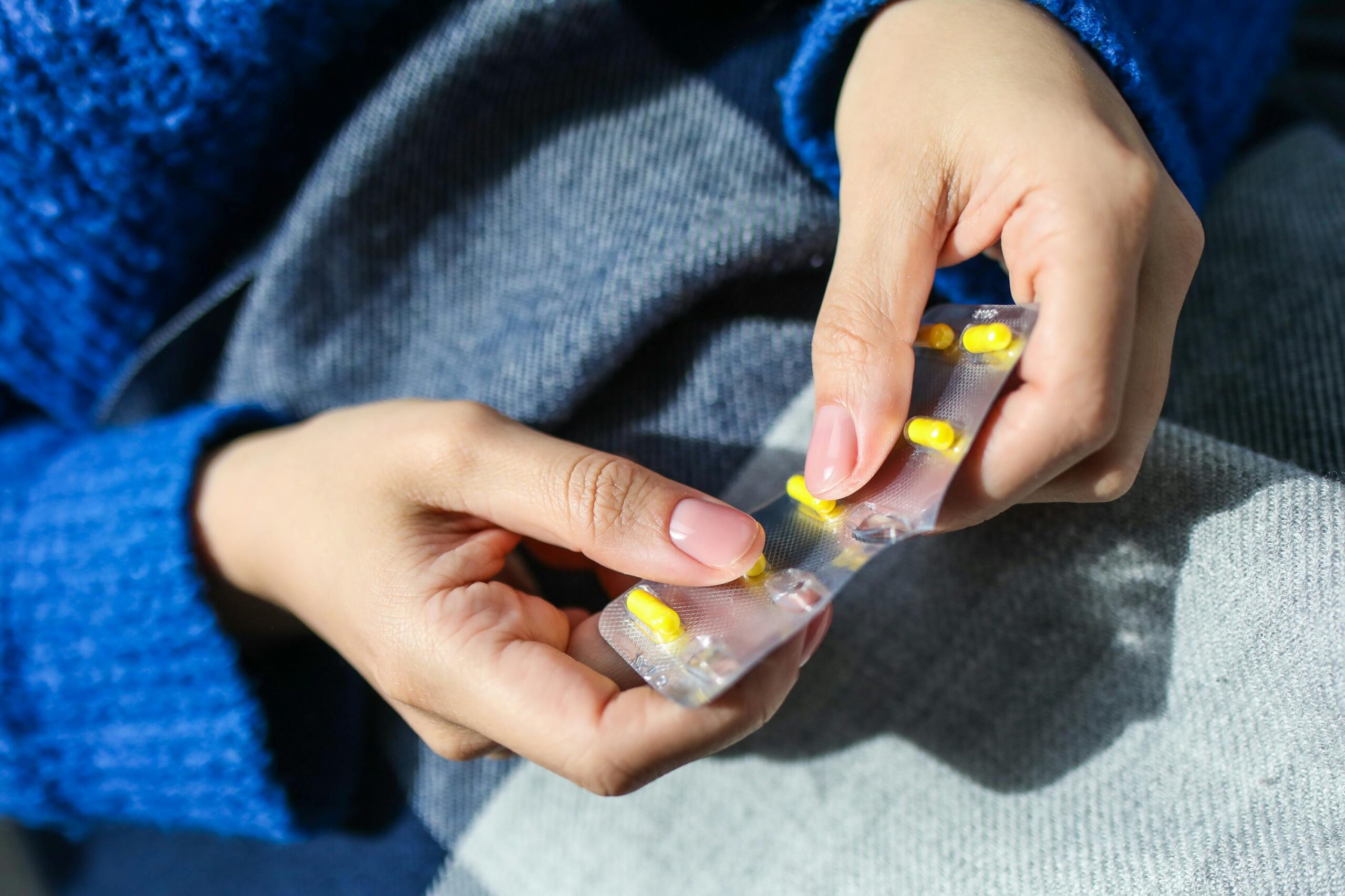 Close-up of a woman's hands holding a blister pack with yellow pills, indoors.