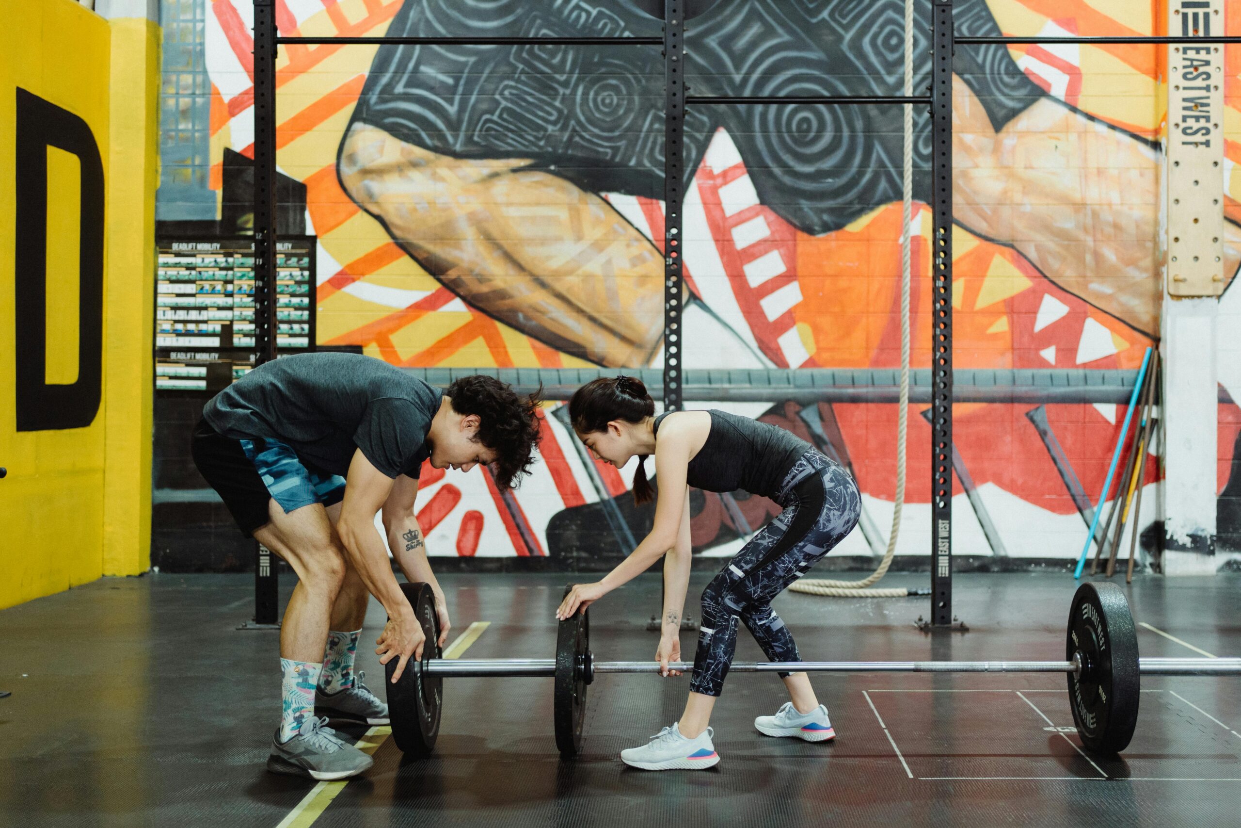 A man and woman lifting weights in a vibrant, artistic gym setting.