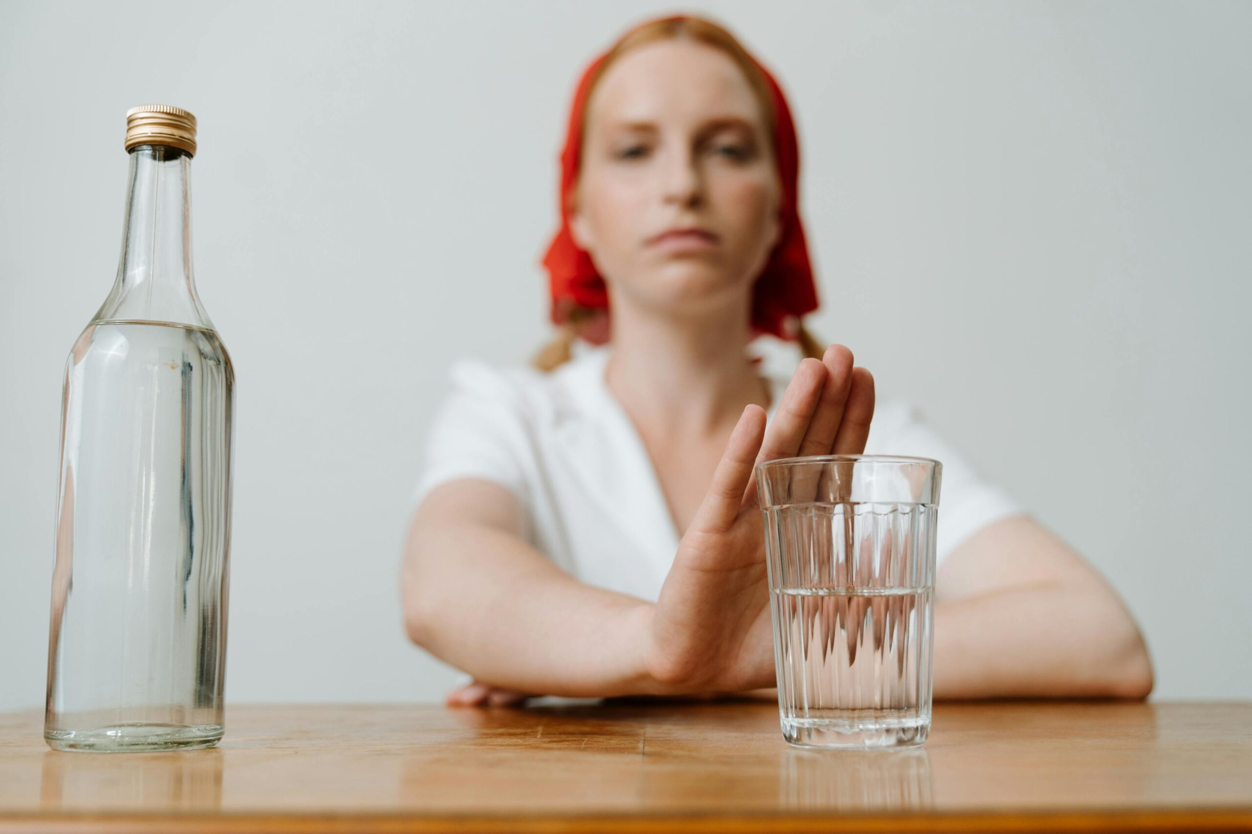 A woman with a red kerchief rejects a glass of alcohol, symbolizing sobriety or refusal.