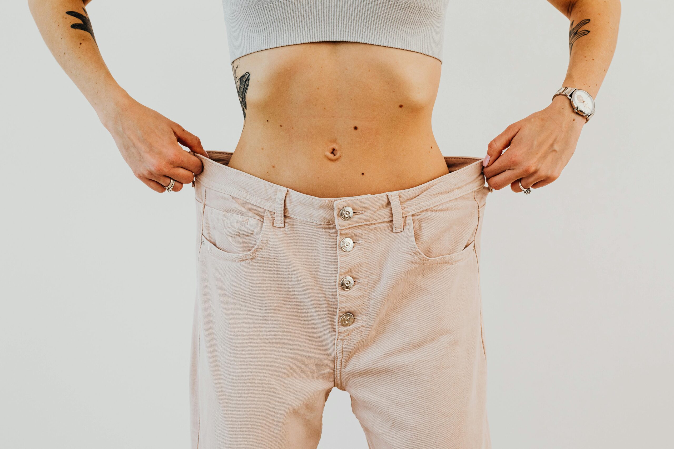 Close-up of a woman holding oversized pants at her waist, showcasing significant weight loss.