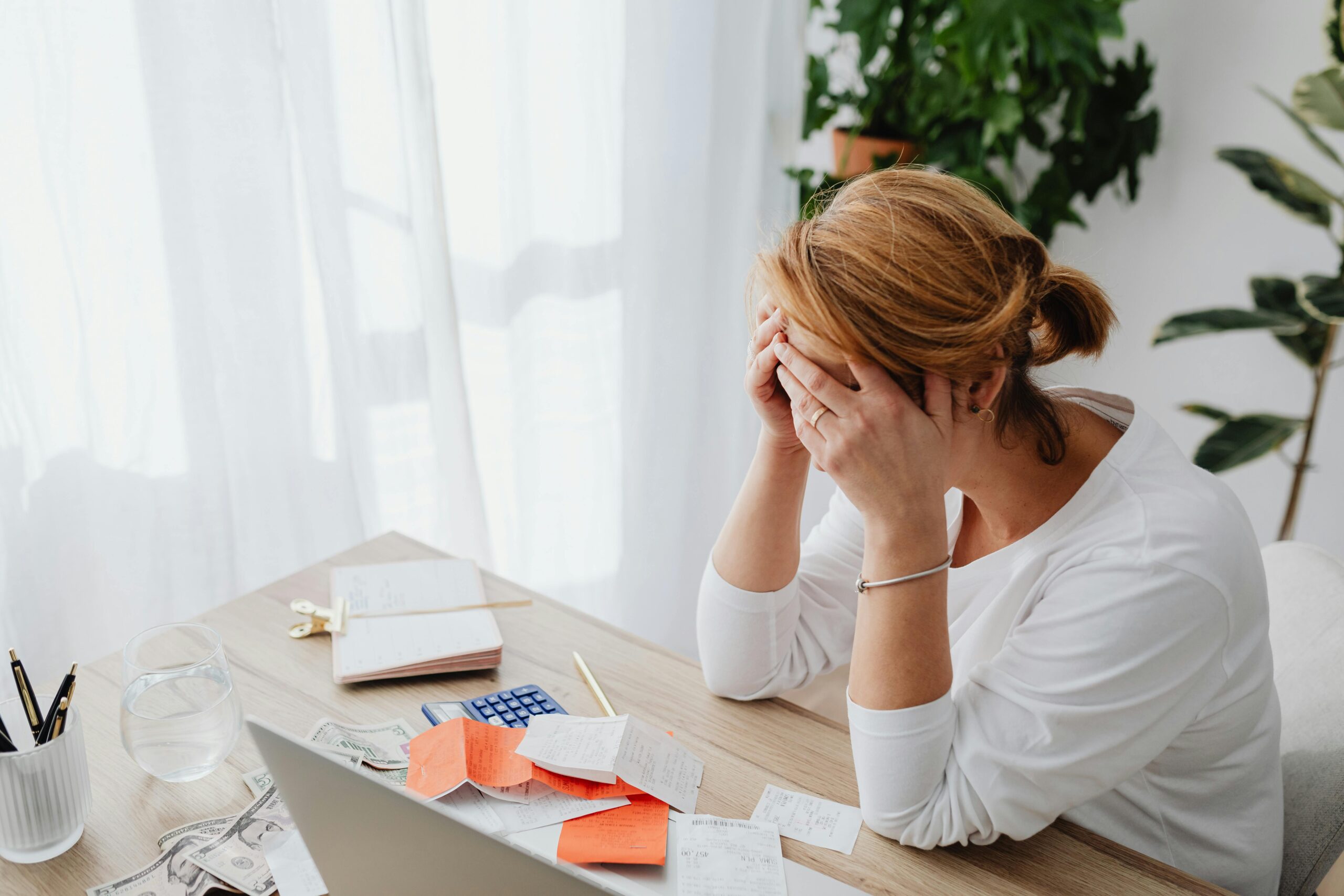 Woman stressed over financial receipts at a desk, dealing with expenses and calculations.