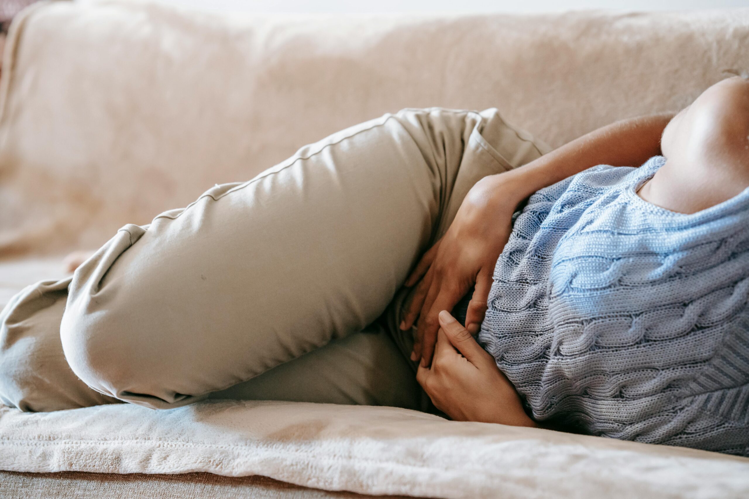 Crop faceless female in casual wear lying on sofa while having acute pain in stomach