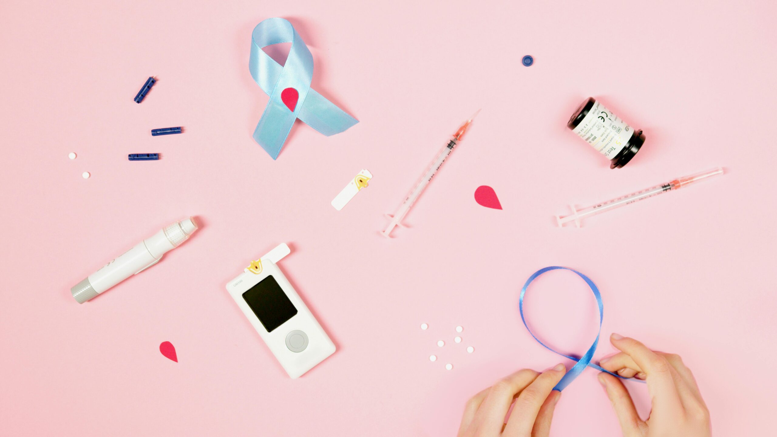 Flat lay of diabetes-related items on pink background emphasizing awareness and healthcare.