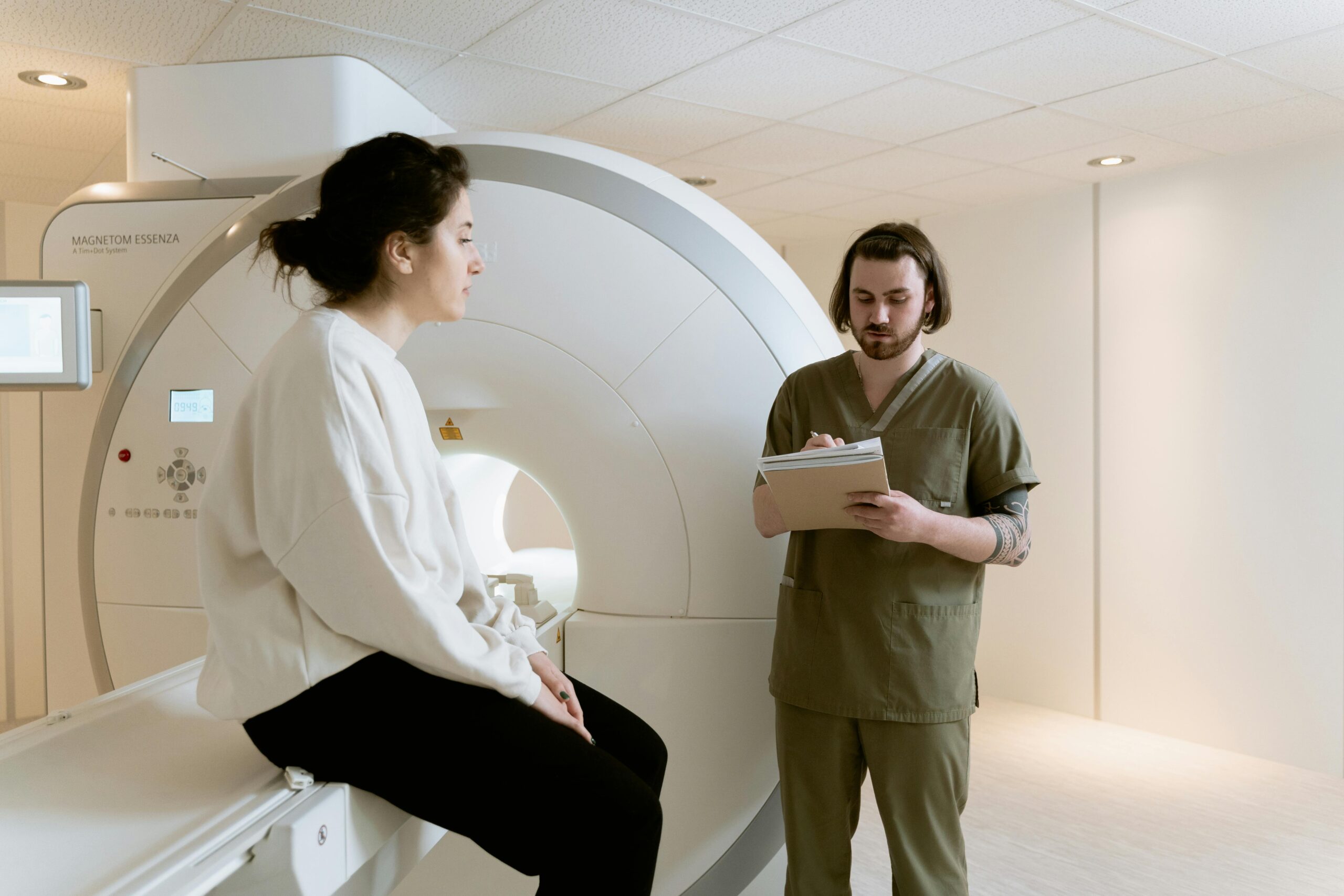 A patient undergoing an MRI scan with a healthcare technician taking notes in a medical facility.