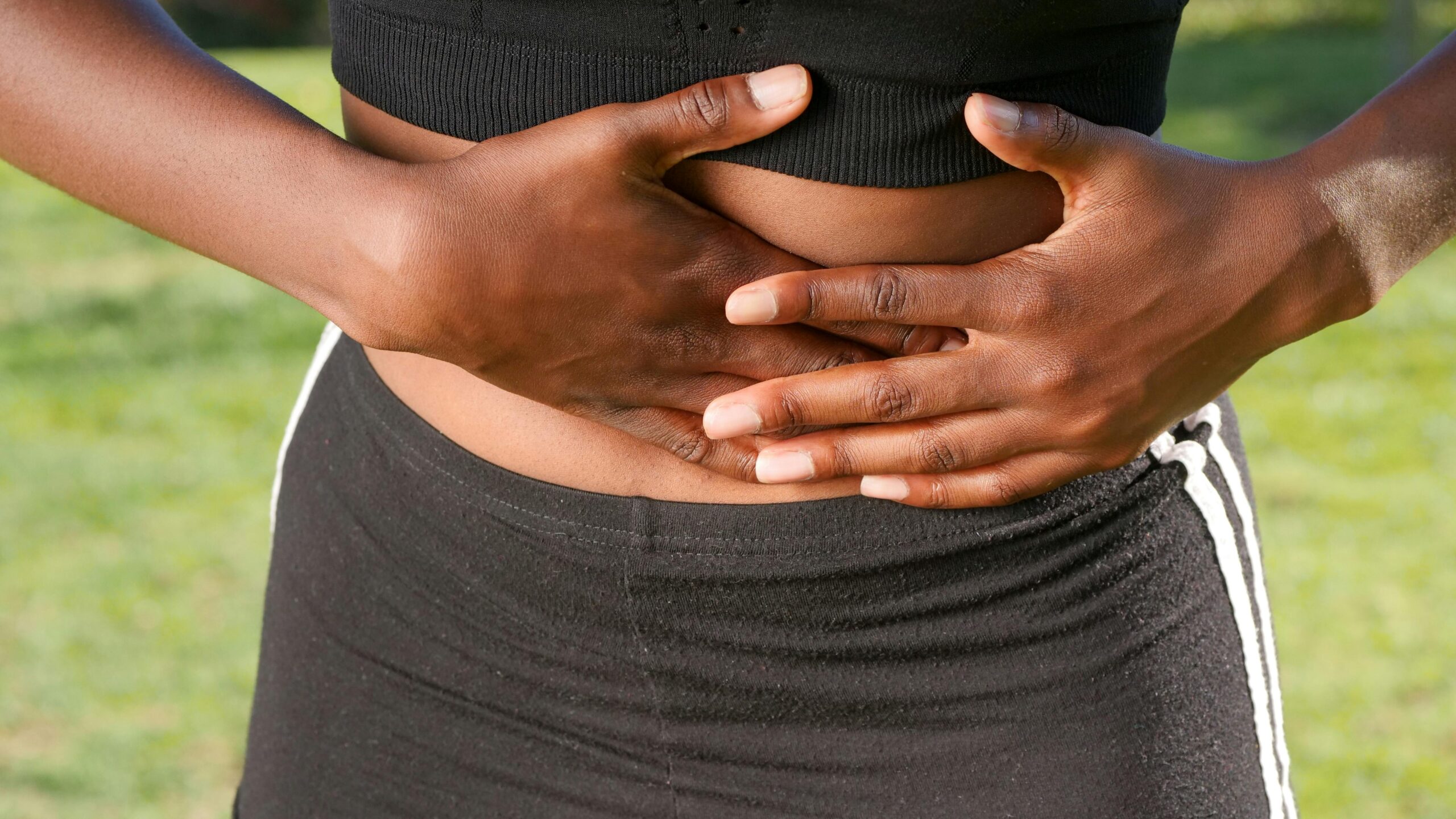 A woman holding her stomach outdoors indicating possible abdominal discomfort or pain.