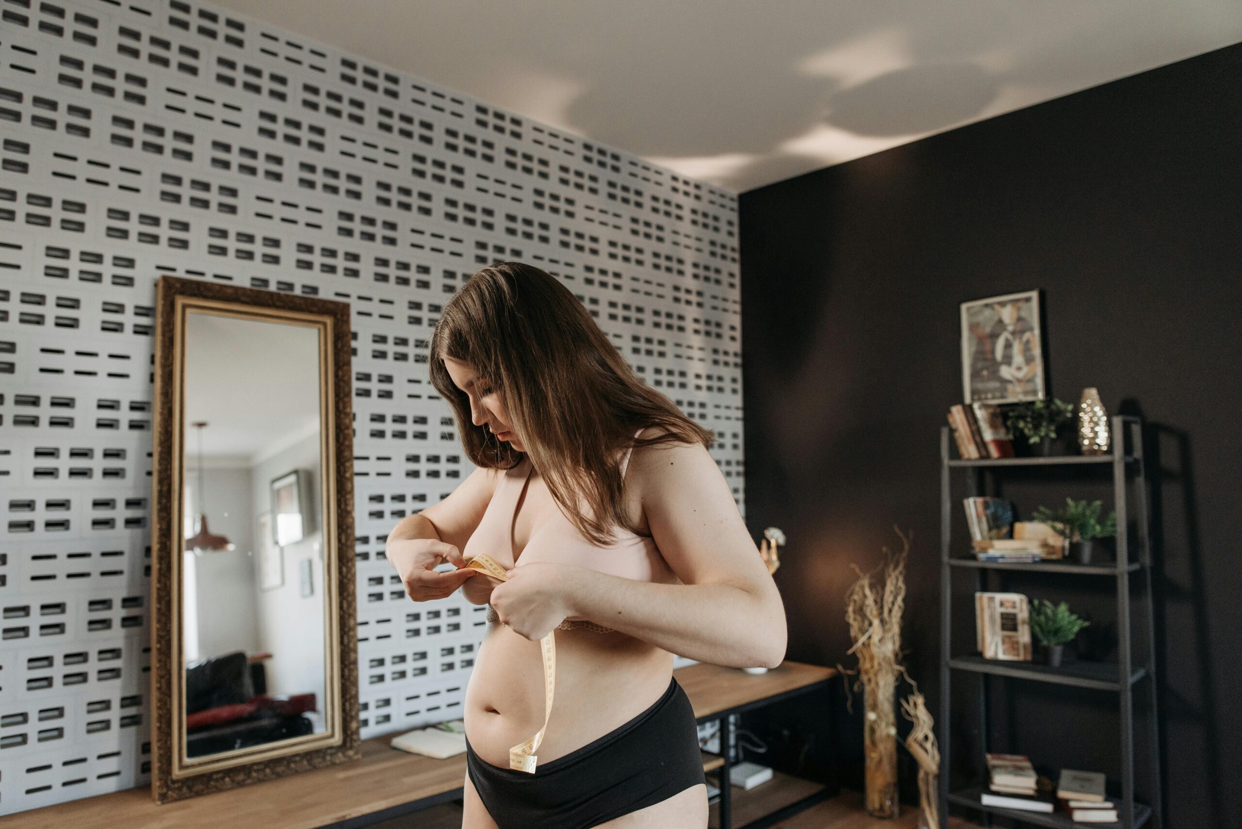 Young woman measuring waist in modern room with mirror, focusing on health and fitness.