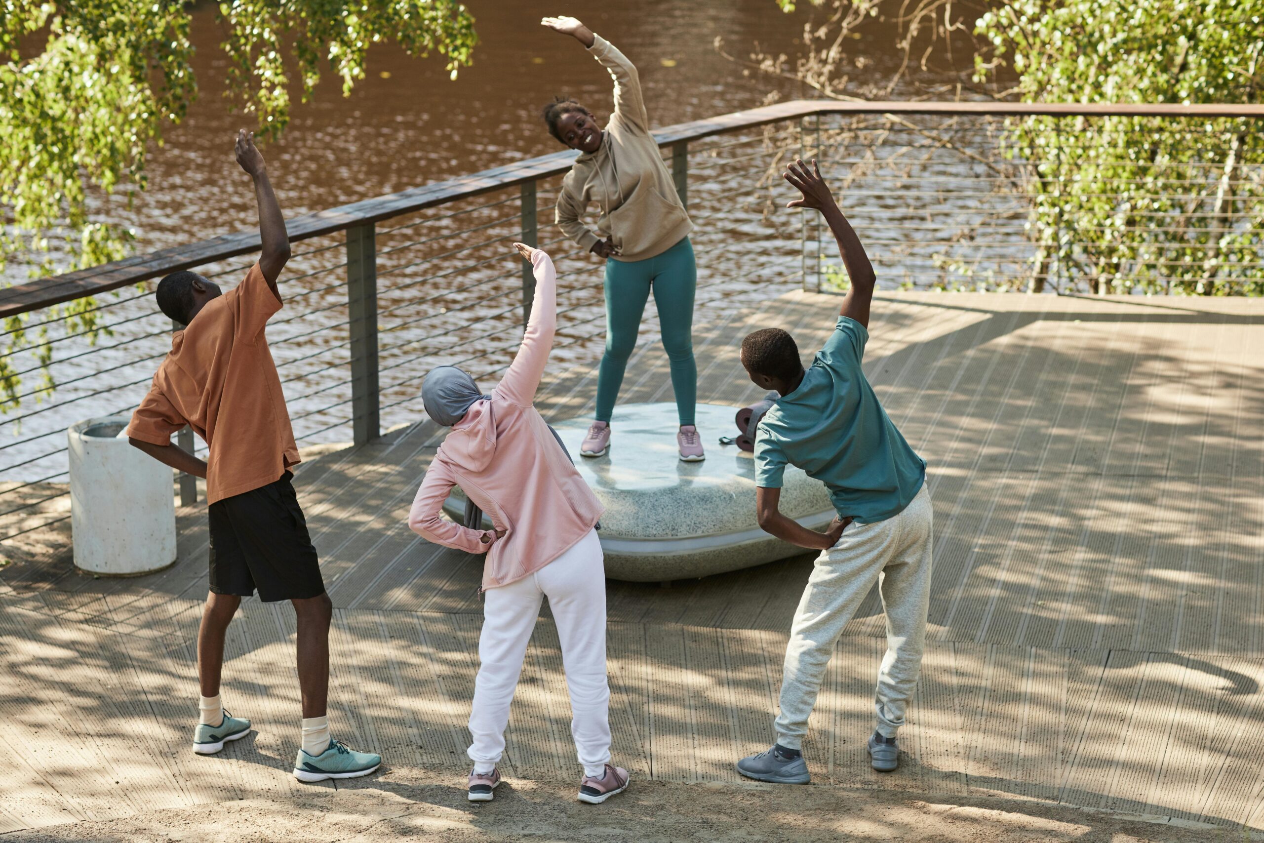 Four adults stretch and exercise outdoors near a riverside park, enjoying a healthy lifestyle.