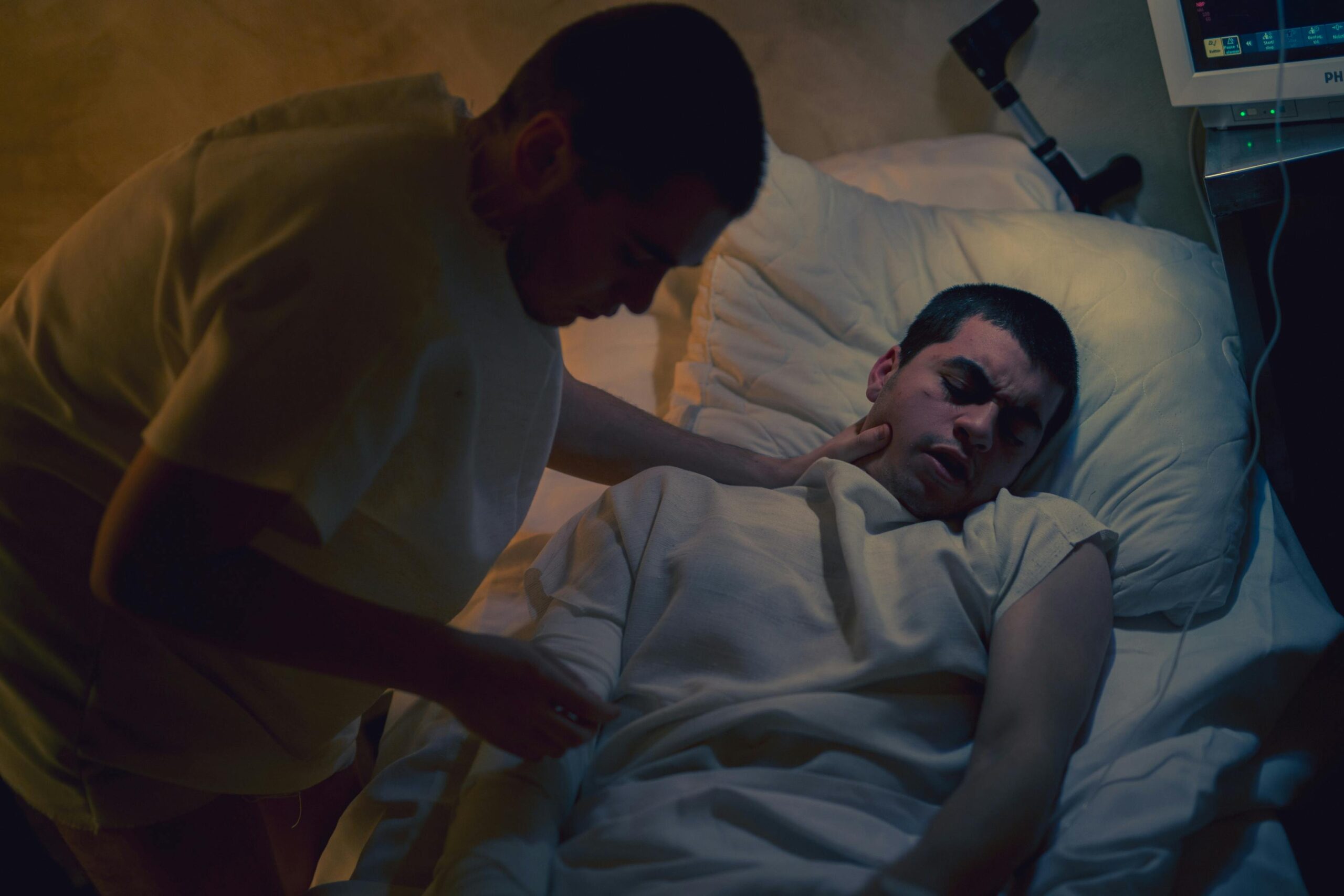 A healthcare professional providing care to a patient lying in a hospital bed under dim lighting.