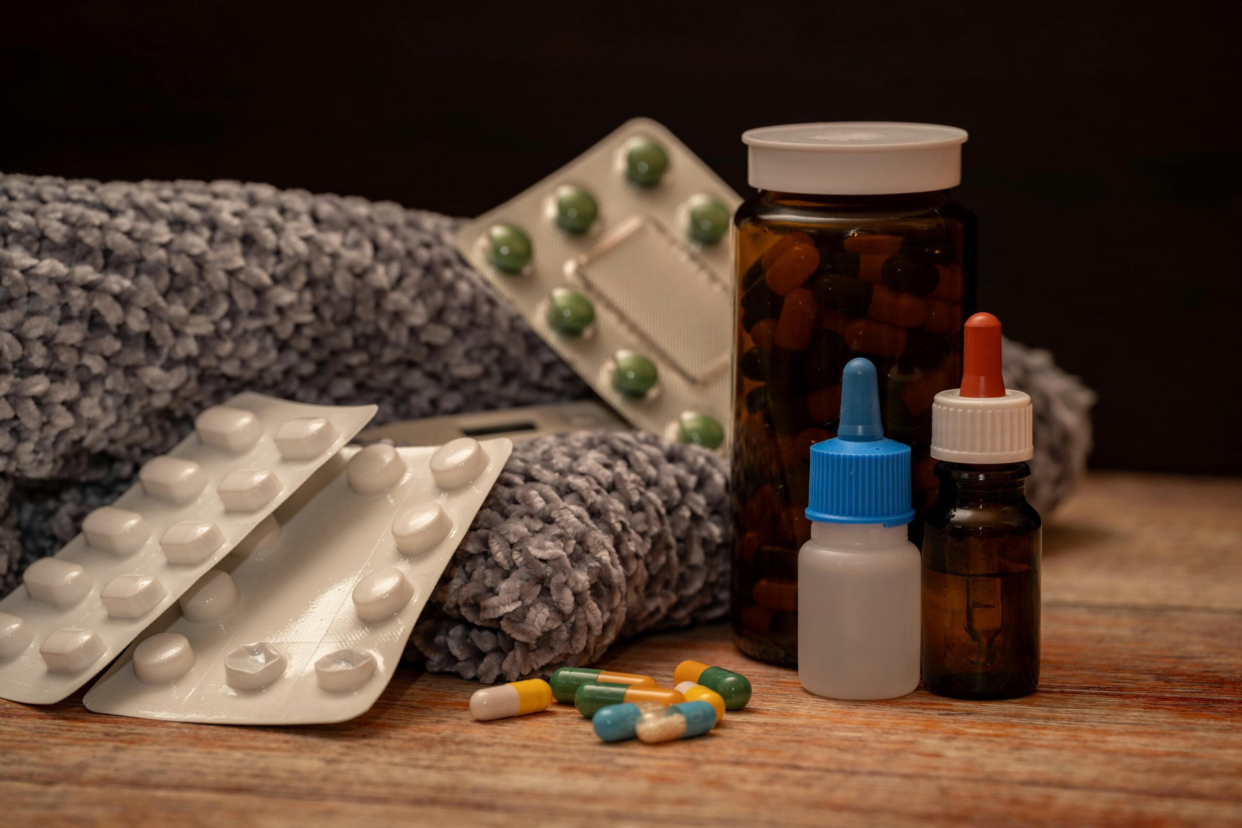 Cold remedies including pills, bottles, dropper, and scarf on a wooden table.