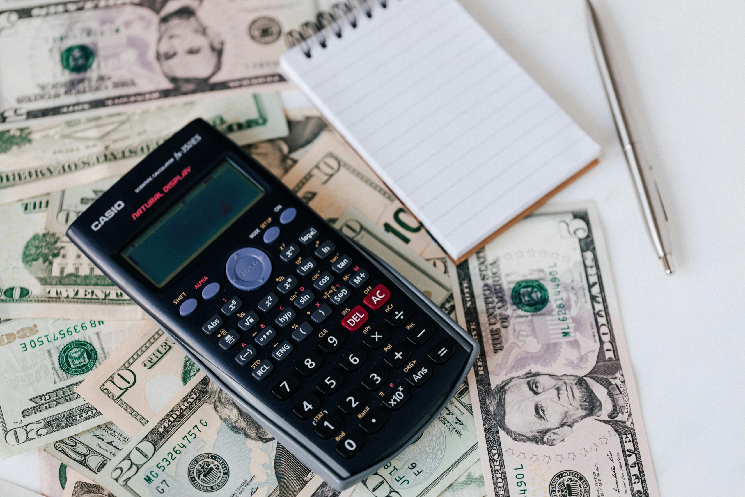 From above electronic calculator and notepad placed over United States dollar bills together with metallic pen for budget planning and calculation.