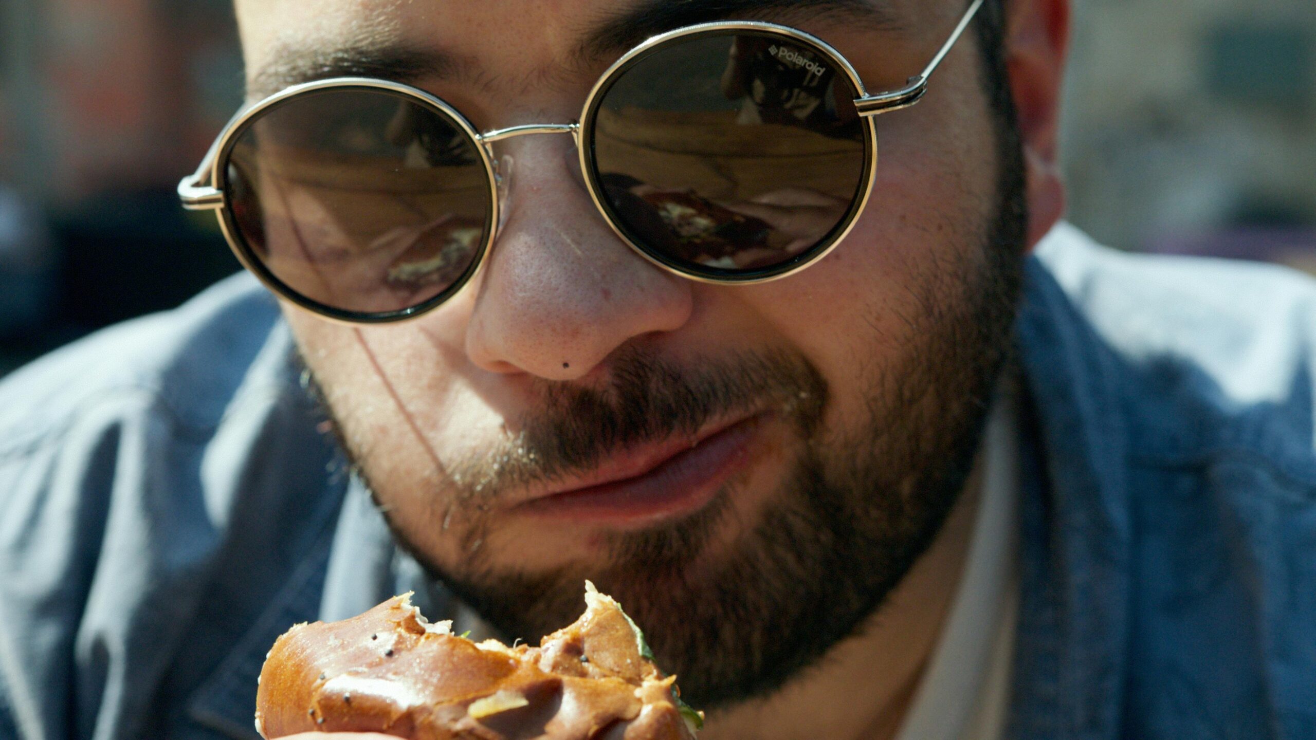 Portrait of a young man wearing sunglasses enjoying a delicious burger outside on a sunny day.