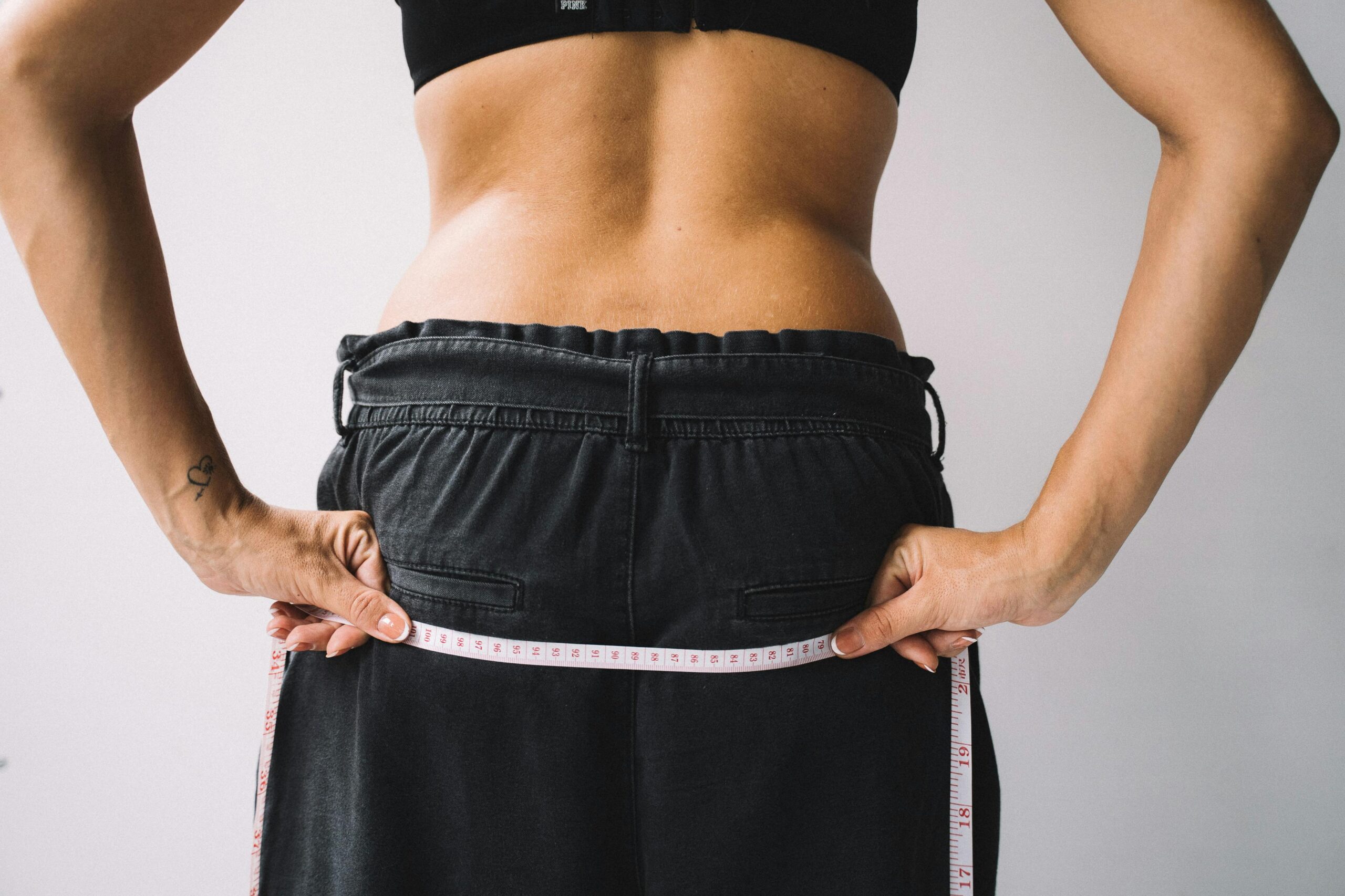 Person measuring their waist with a tape measure, symbolizing fitness goals.