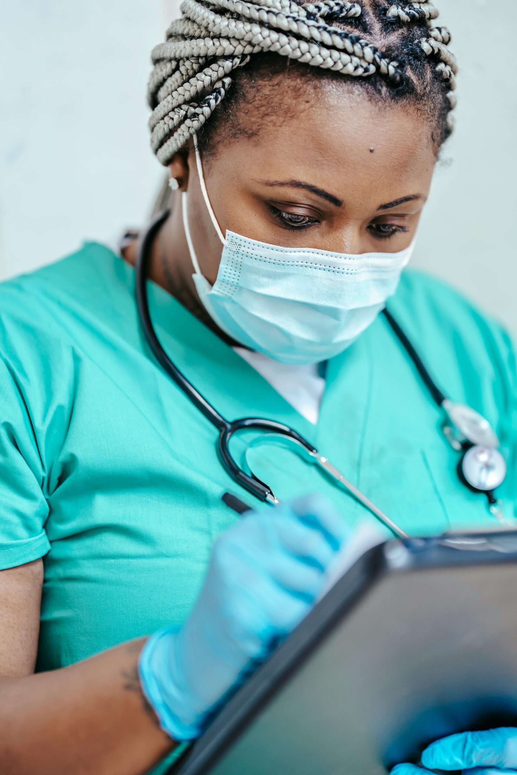 Nurse with mask and gloves reviewing documents on clipboard in a clinic setting.