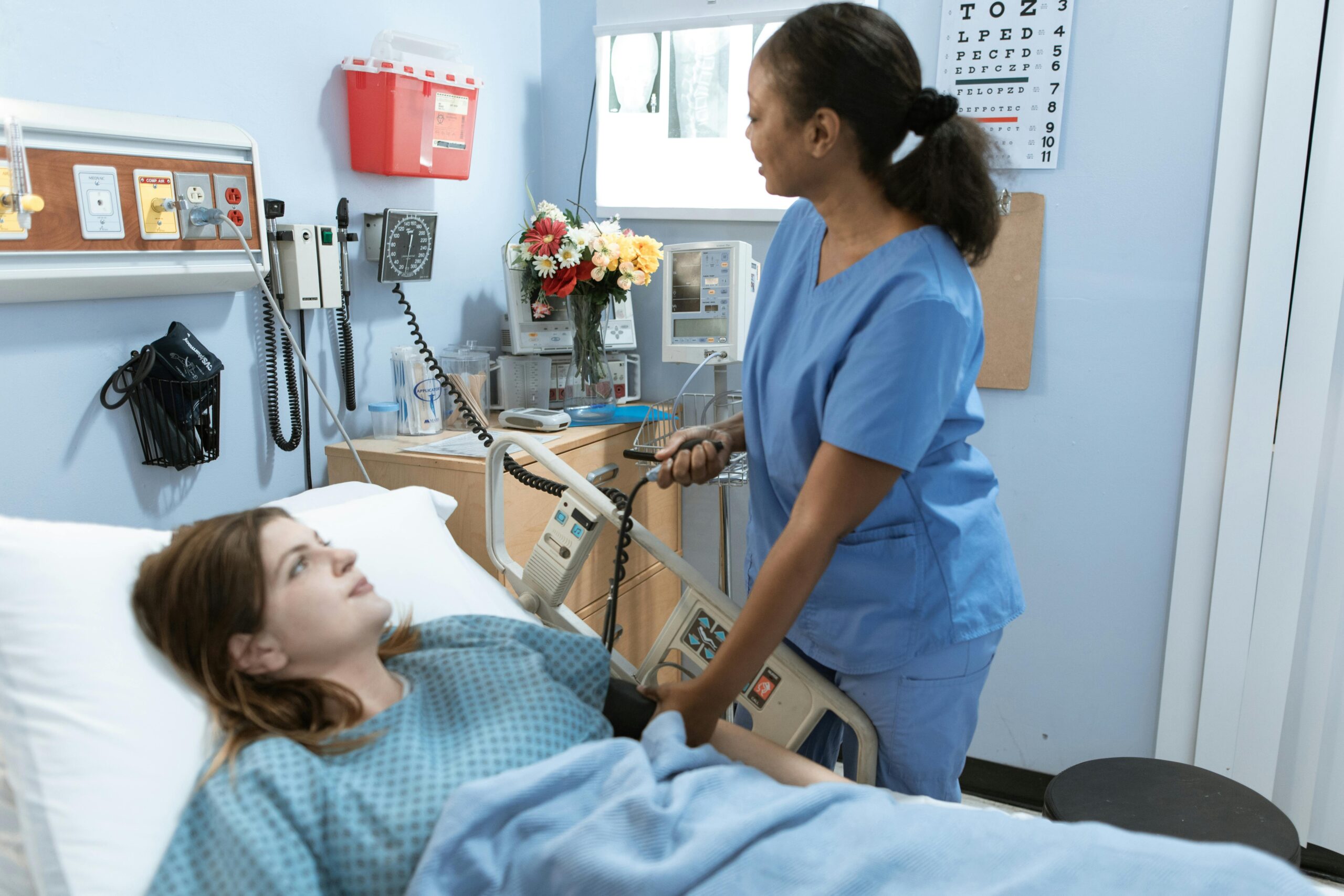 Nurse providing care to a patient in a hospital room with medical equipment.