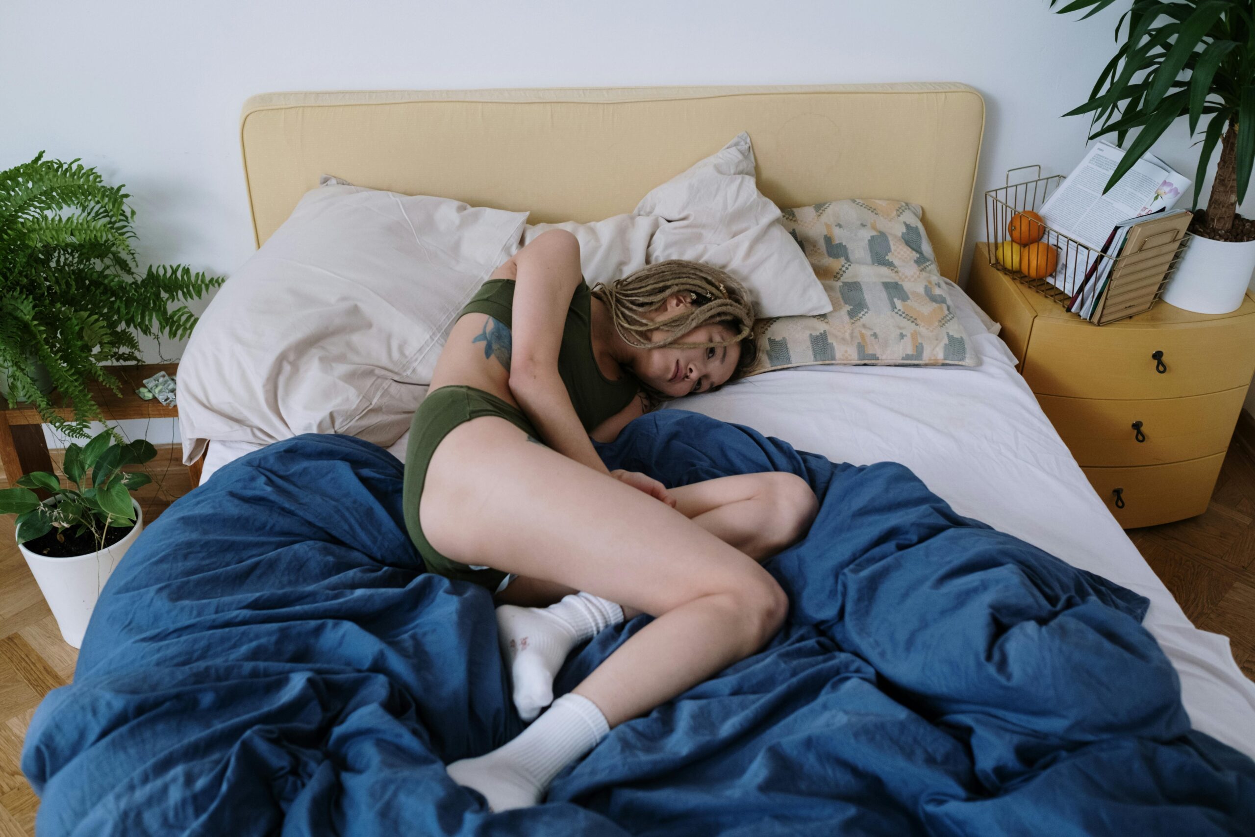 Woman lying in bed experiencing abdominal discomfort surrounded by cozy interior.