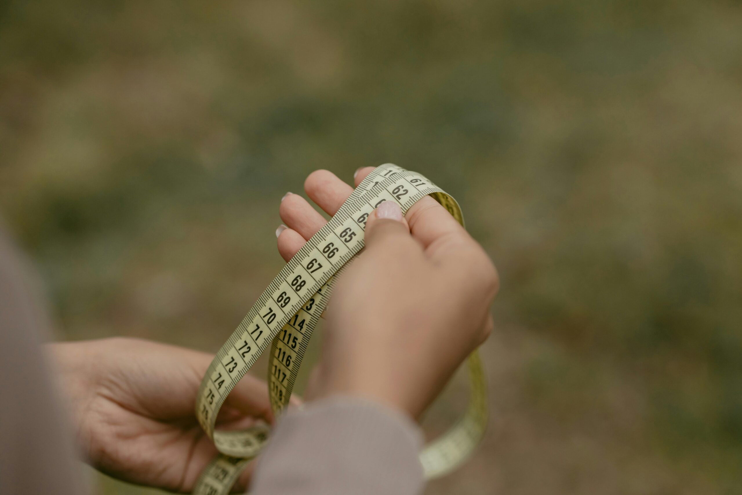 Hands holding a rolled measuring tape, focused on numbers and markings.