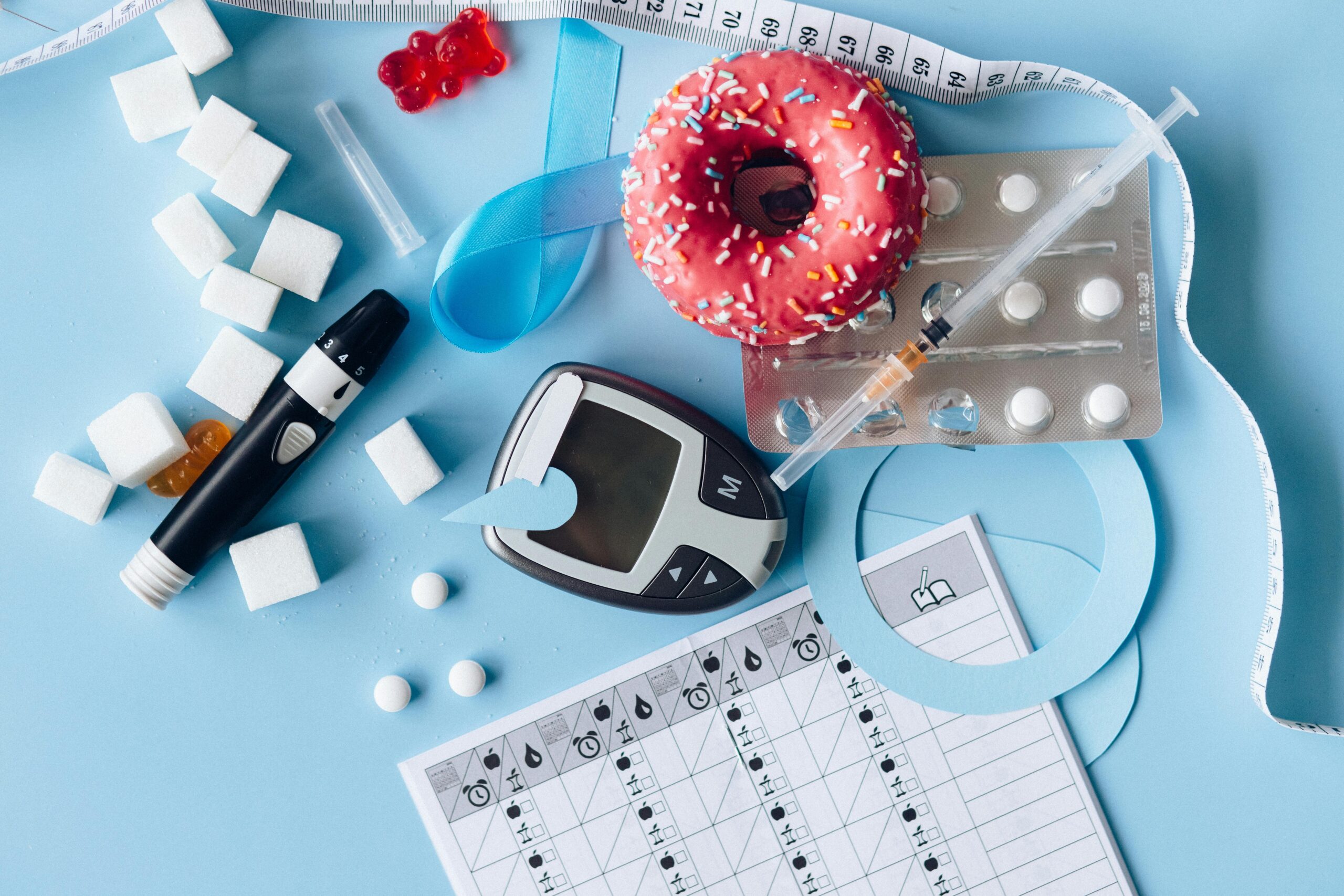 Still life image of diabetes management equipment, sweets, and medication arranged artfully on a blue background.