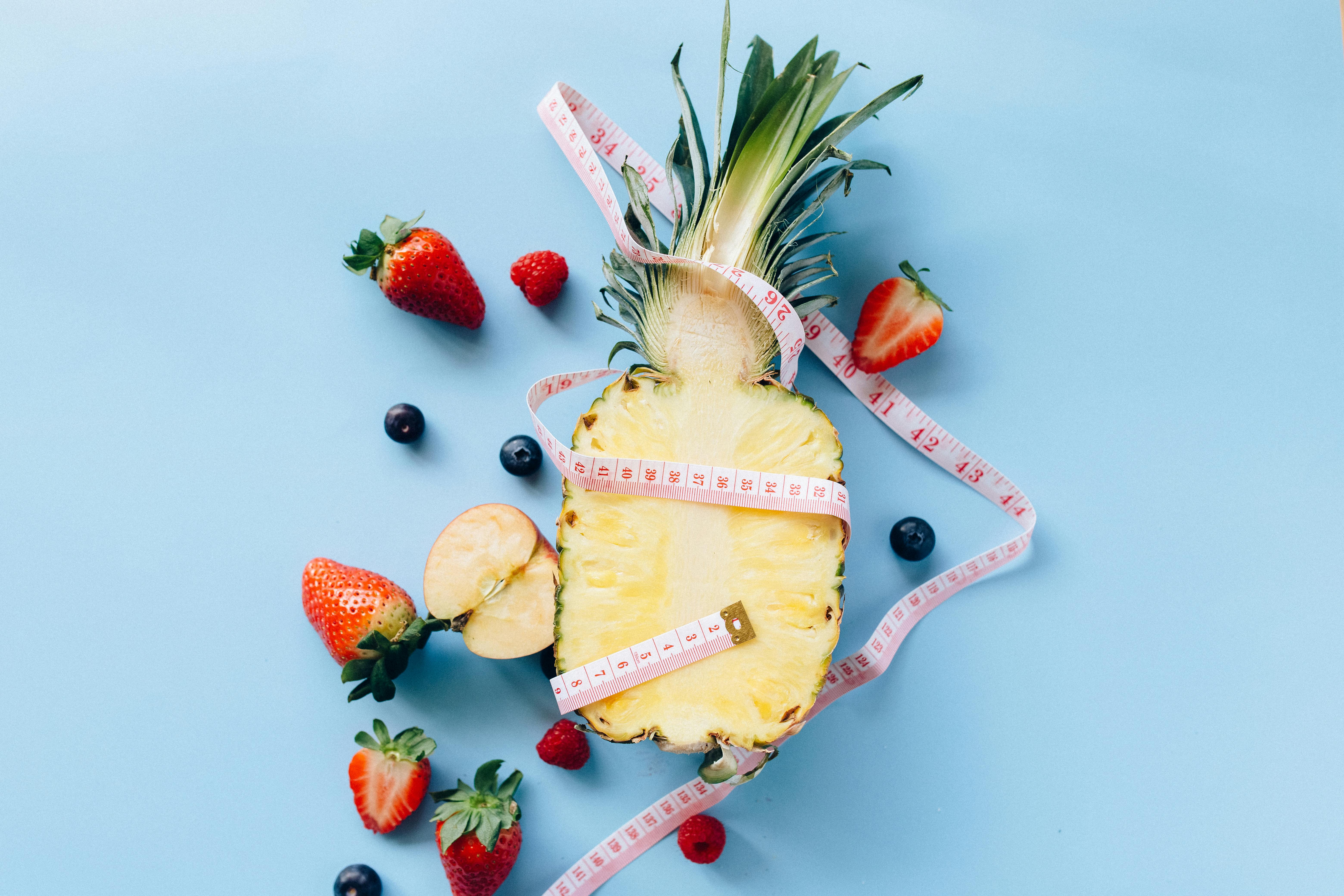 Fresh fruits with tape measure on blue background symbolize healthy lifestyle and nutrition.