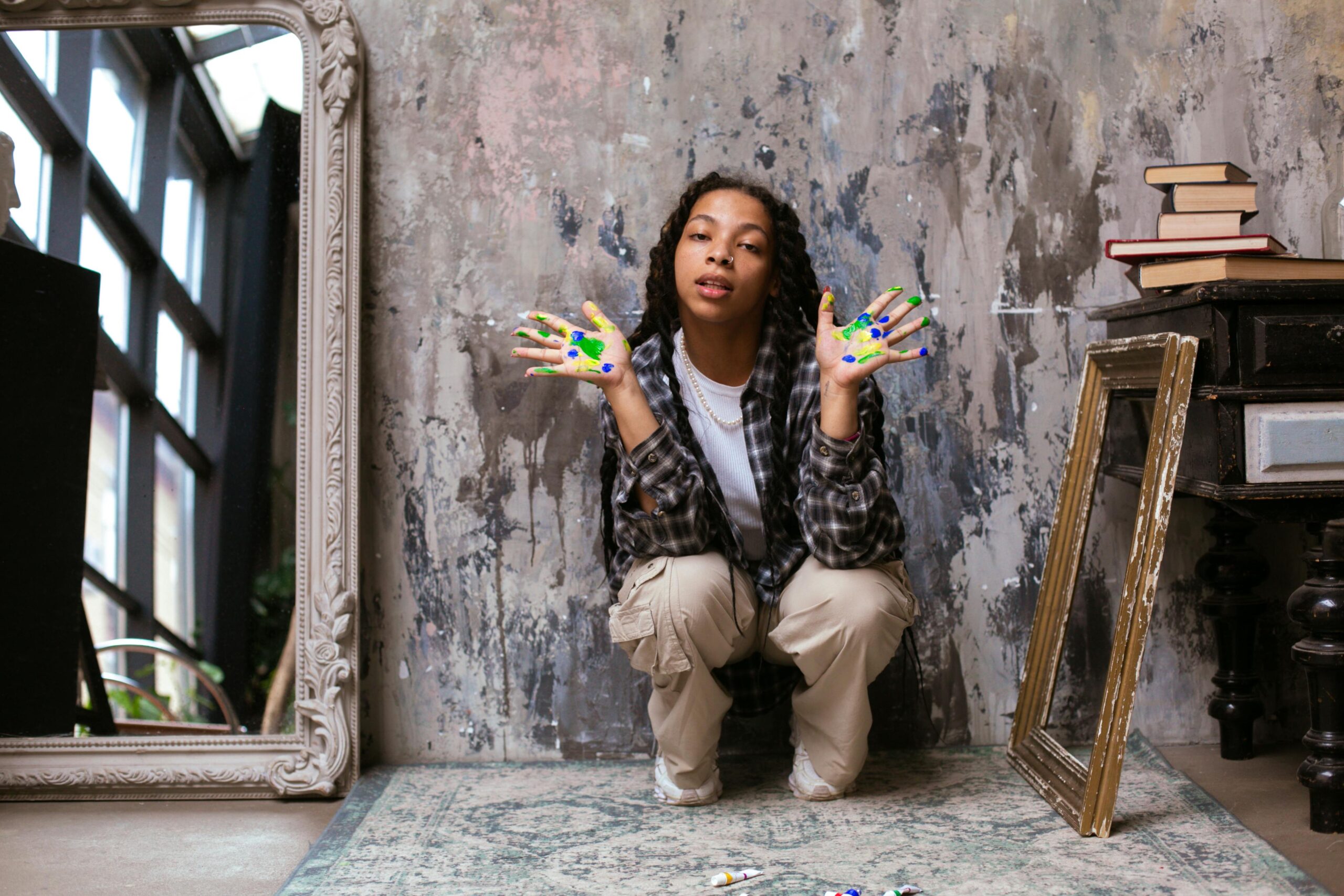 Teen girl with paint-stained hands crouching in an artistic studio showcasing creativity.