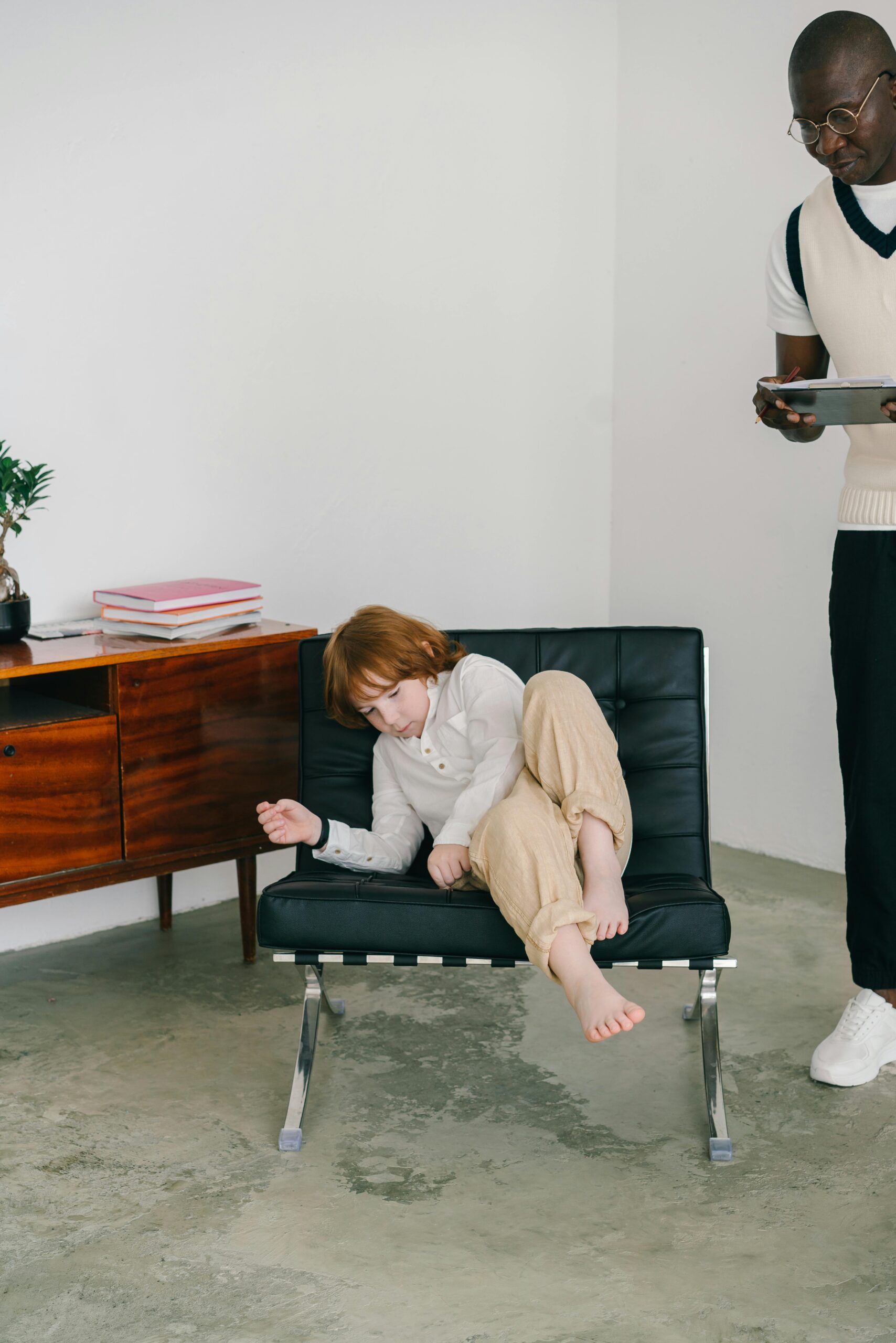 A child rests during a therapy session with a psychologist holding a tablet.