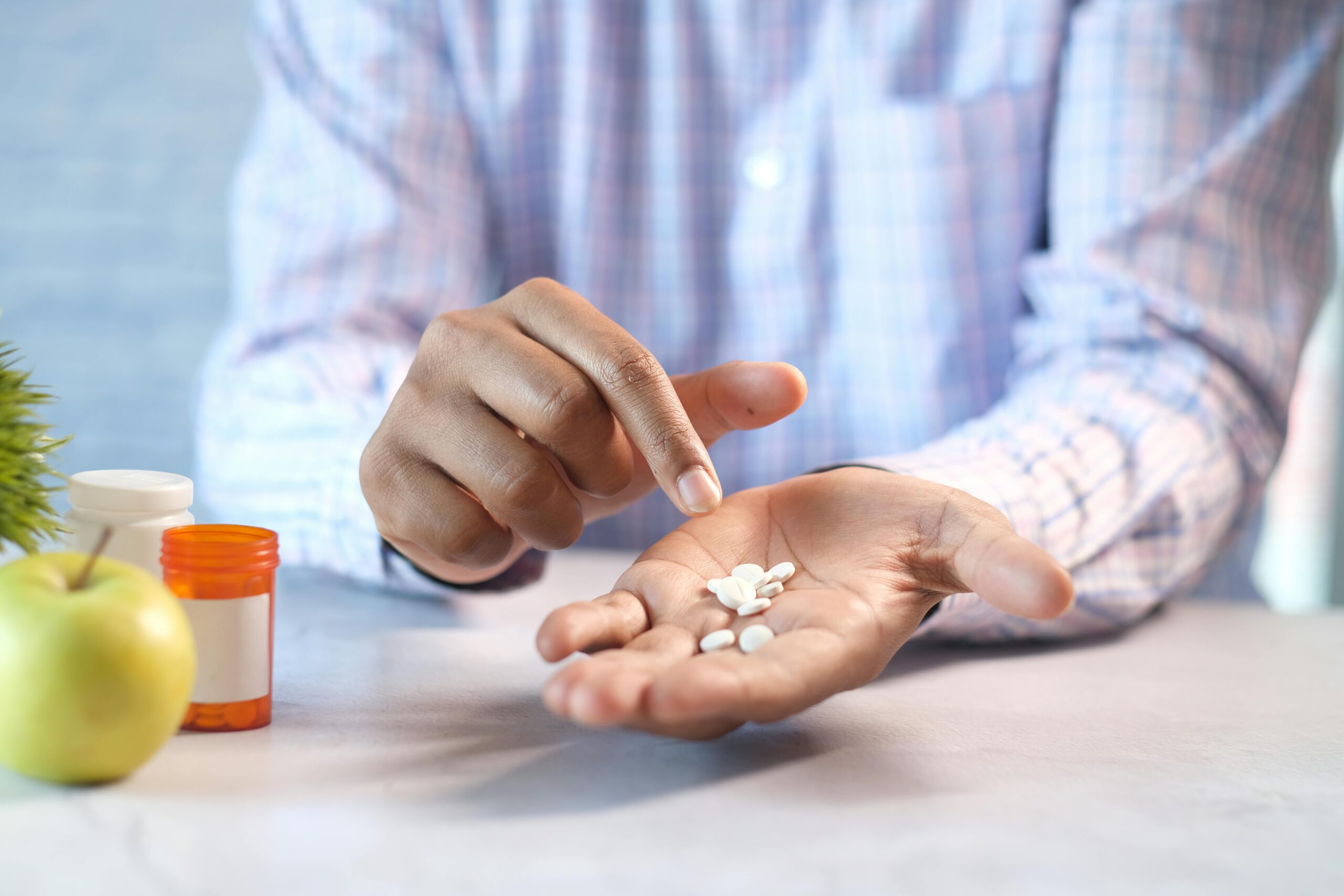 Close-up of a man's hands holding and pointing at white pills next to a prescription bottle.