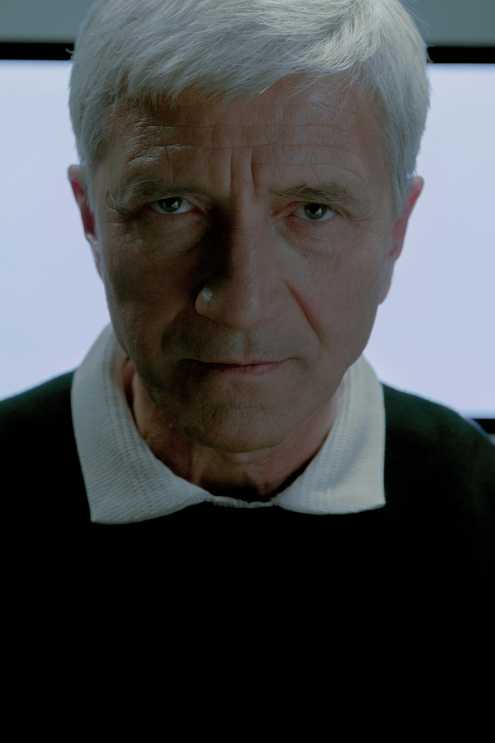 Introspective portrait of a senior man with grey hair looking directly at the camera.