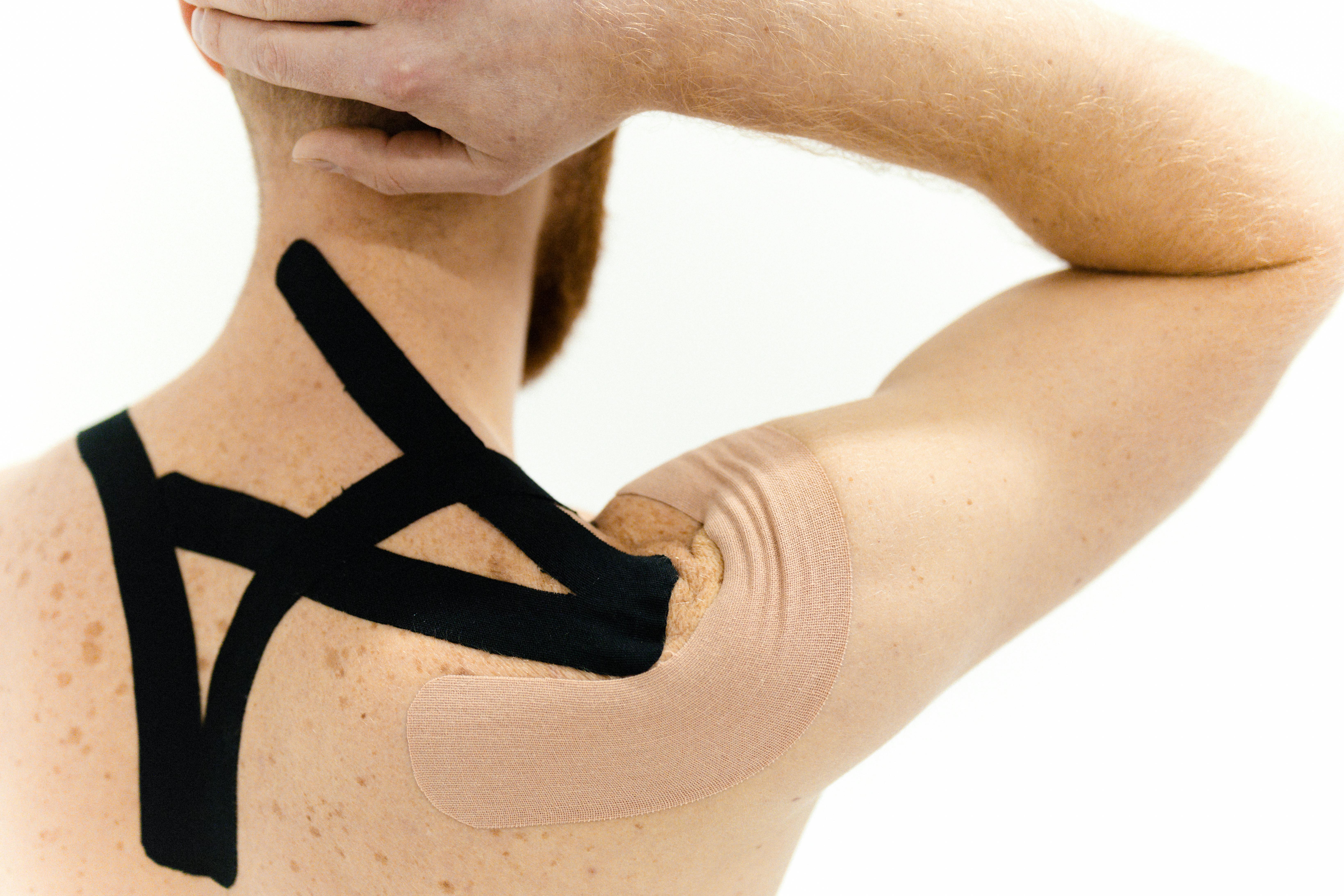 A man with kinesiology tape applied on his shoulder against a white background, showcasing physical therapy support.