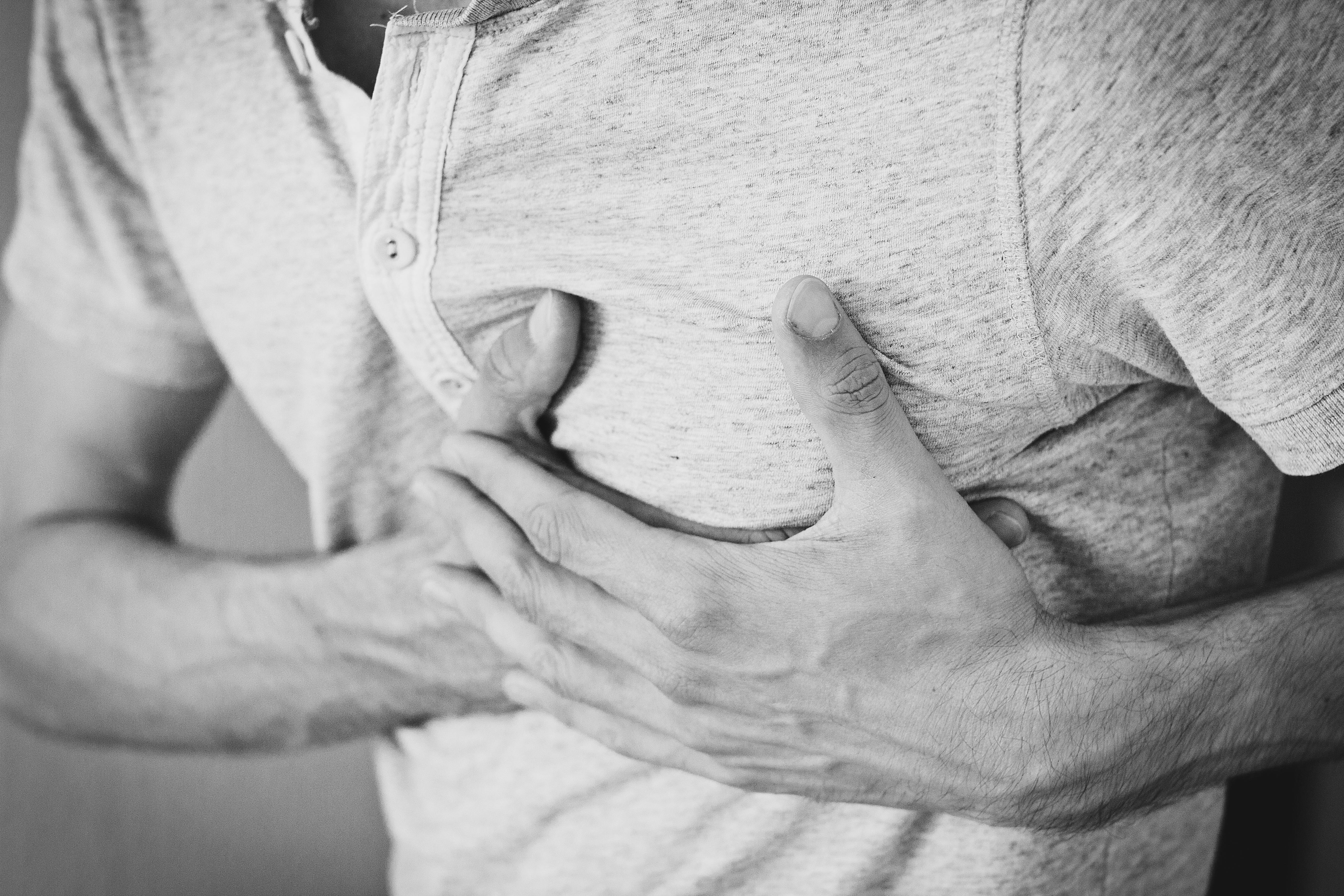 Black and white photo of a man clutching his chest, indicating discomfort or pain.