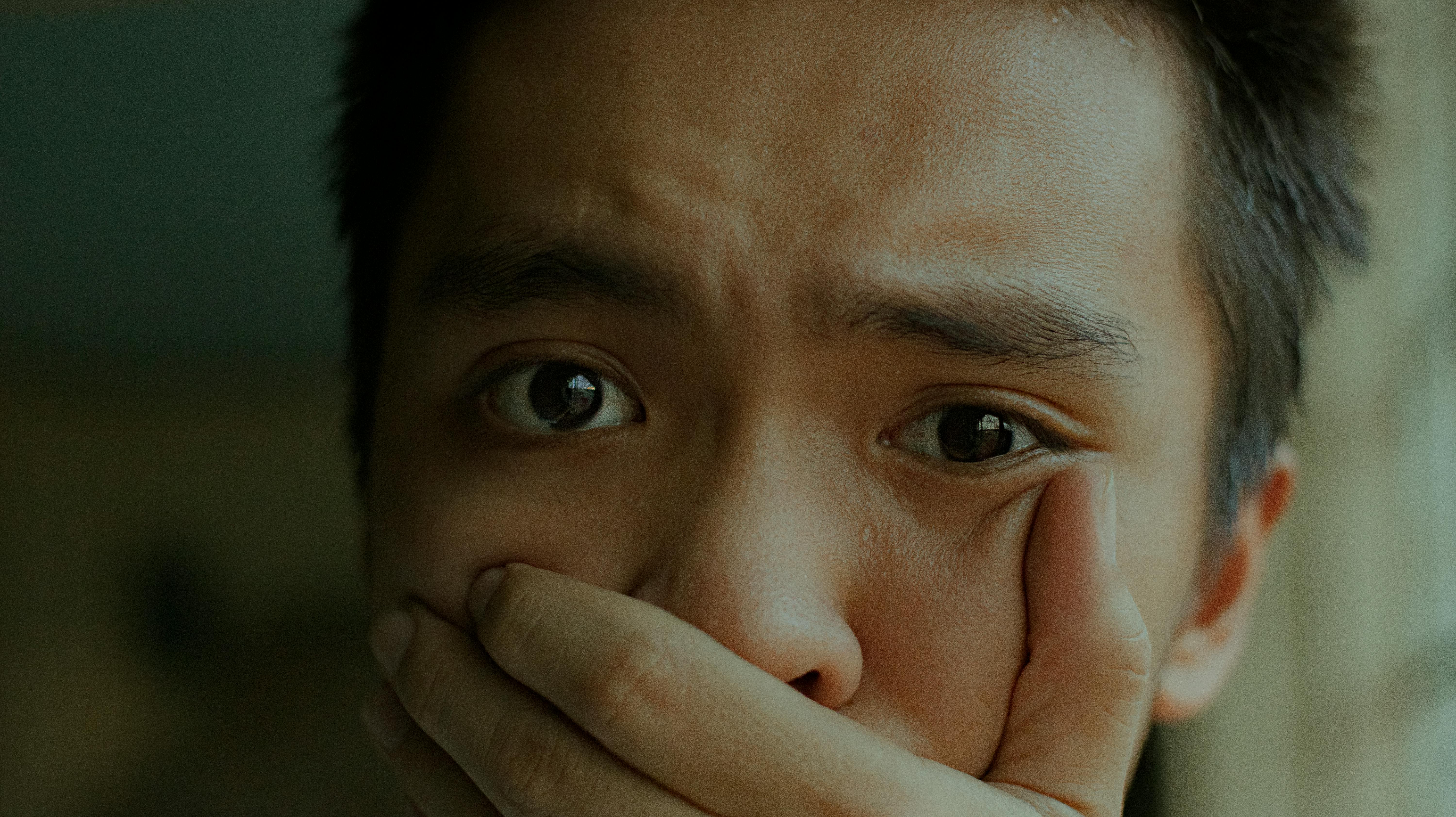 A young man with a distressed expression, covering his mouth.