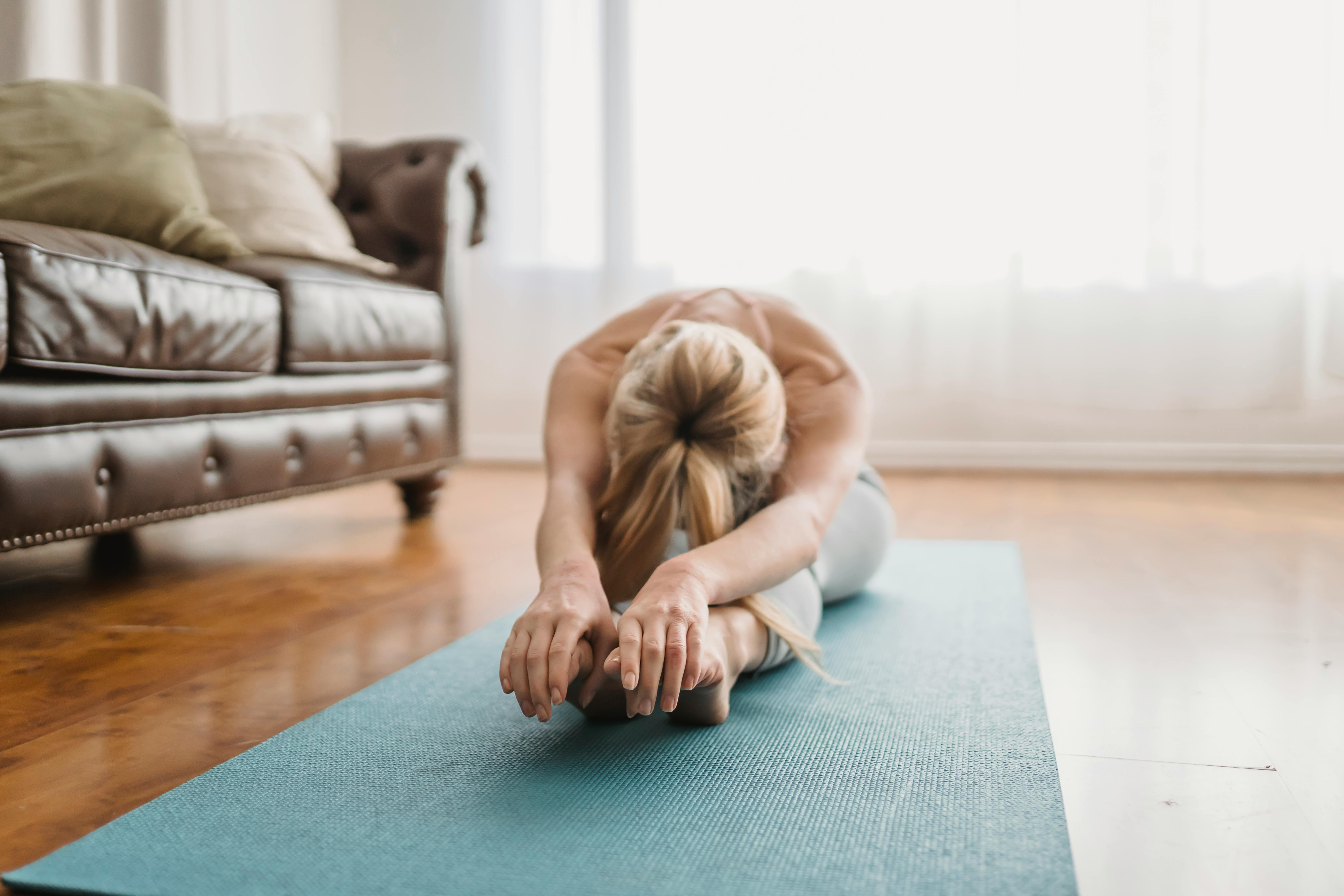 A woman performs a yoga stretch on a mat in a cozy living room, embracing wellness and relaxation.