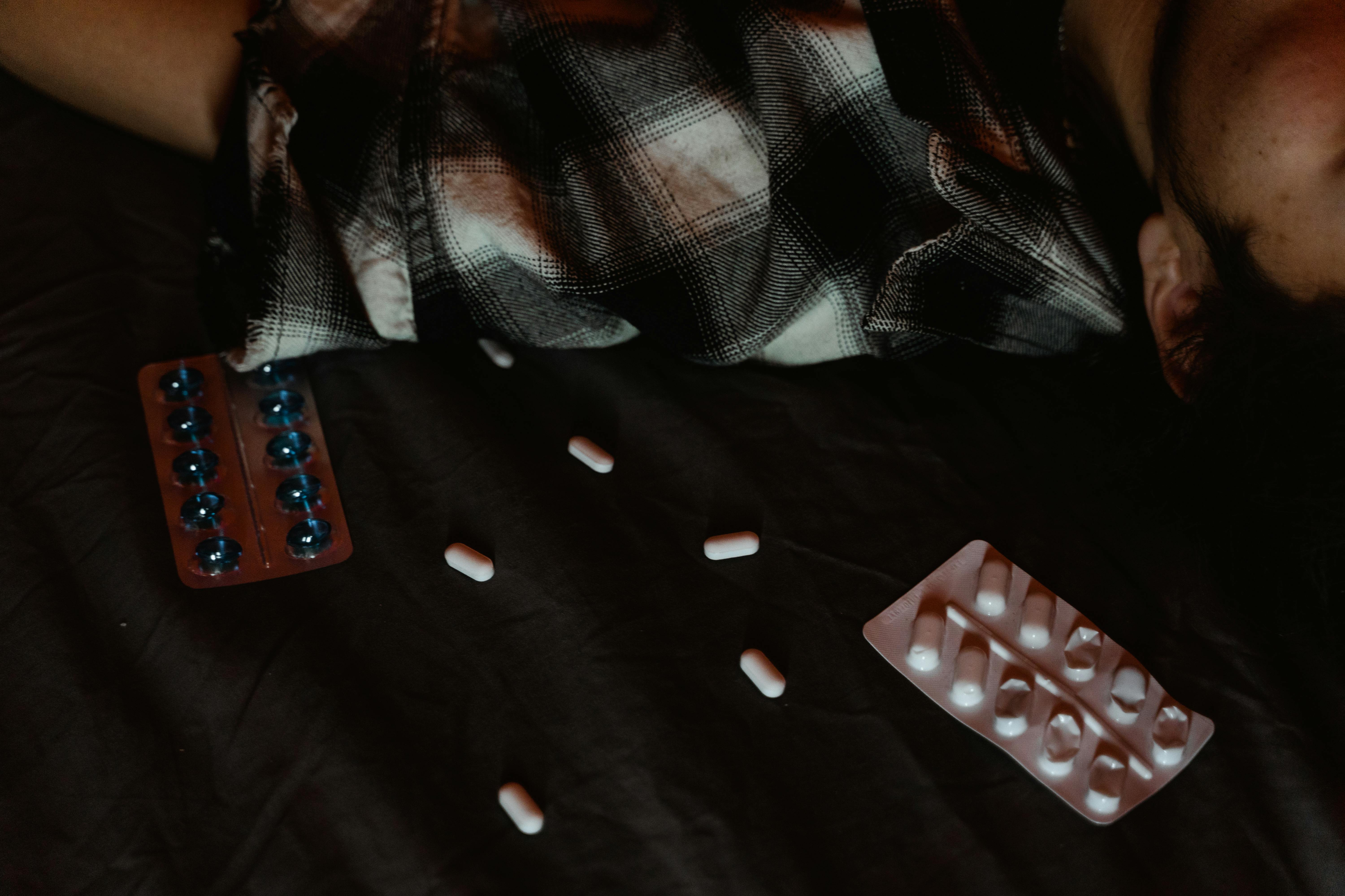 Dark scene with pills scattered near a person, suggesting themes of mental health and medication.