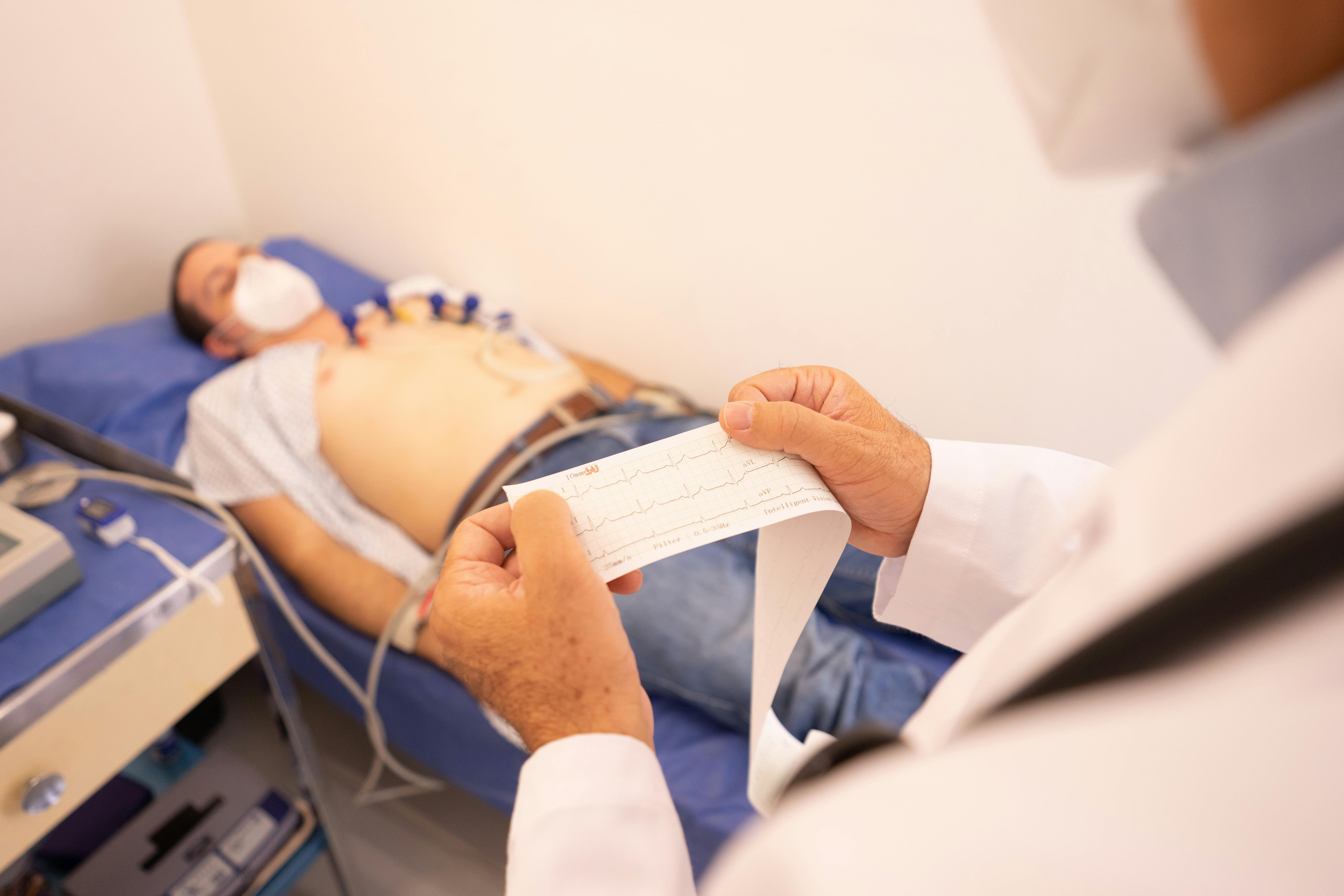 A doctor analyzes an ECG printout while a patient undergoes monitoring in a medical clinic.